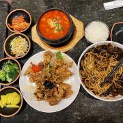 Black bean noodles, soft tofu soup, pork, and side dishes on a black table. 