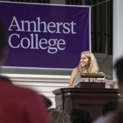 A woman speaking at a podium with a banner saying Amherst College in the background