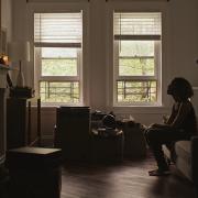 A woman sitting in a dark living room in front of two windows