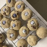 Image shows chocolate chip cookies cooling on a wire rack with purple m&ms embedded in the cookie