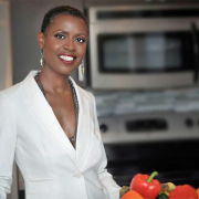 A Black woman in a white suit jacket standing in a kitchen