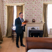 A man reading a book standing in an old-fashioned bedroom