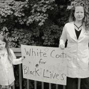 A woman in a doctor's coat and a young child holding a sign that reads "White Coats for Black Lives"