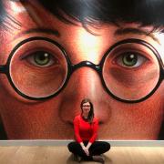 A woman sitting in front of a wall with a the face of Harry Potter looking out at the camera