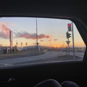 Image shows a pink, yellow, and blue sunrise being framed by a car window.